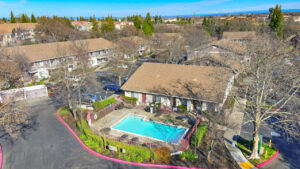 Exterior aerial of woodcreek terrace clubhouse and community pool, surrounding residential buildings in background, meticulous landscaping around buildings.