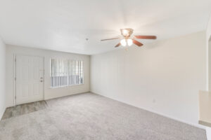 Interior Unit Living Room, Neutral toned carpeting, overhead lights/fan, window to the right of entry door, ceiling fan/ light fixture.