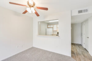 Interior Living Room, neutral toned carpeting, overhead fan in living room, breakfast bar joined to kitchen, white walls.